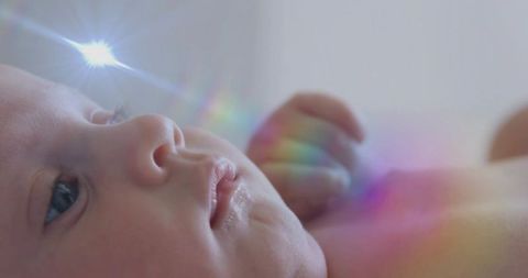 Newborn girl gazing at prism light with rainbow flare, dreamy closeup portrait for nursery