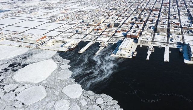 Aerial winter harbor meeting drifting ice floes and steam plumes at snow-covered docks