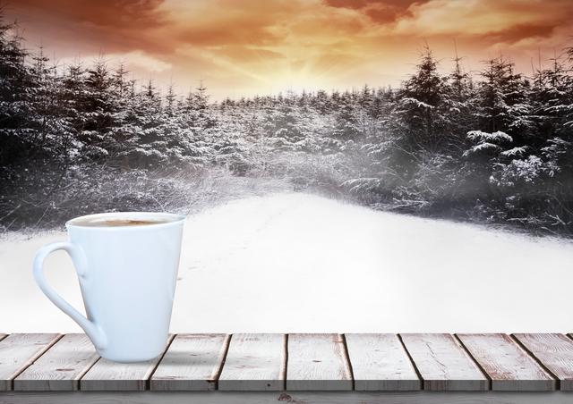 The composition shows a steaming white coffee mug on a wooden plank with a snow-covered forest in the background highlighted by a stunning sunset. Suitable for promoting warm winter beverages, coffee shop advertisements, holiday season marketing, or inspirational winter scenes.