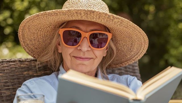 Relaxed Senior Woman Reading Outdoors Wearing Straw Sunhat and Orange Sunglasses