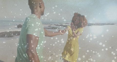 Sunlit beach couple dancing and reaching hands amid dreamy bokeh particles