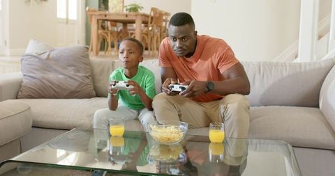 African American father and son intensely playing video games on living room couch