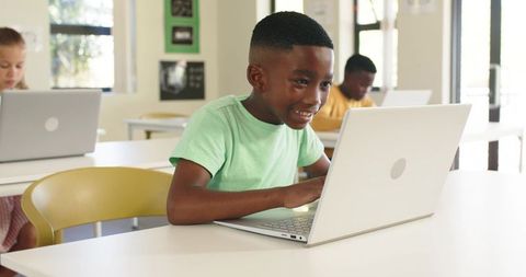 Smiling student typing on laptop in bright classroom during digital learning session
