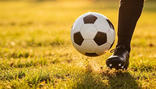 Right-foot kicking soccer ball on sunlit grass at golden hour with turf spray and motion