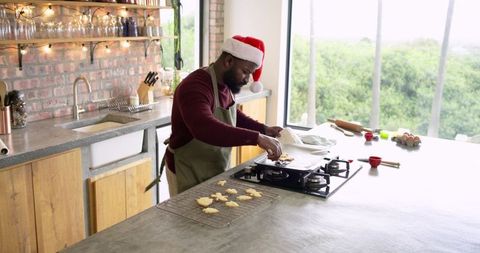 Mid-adult African-American man wearing Santa hat apron baking holiday cookies on kitchen island