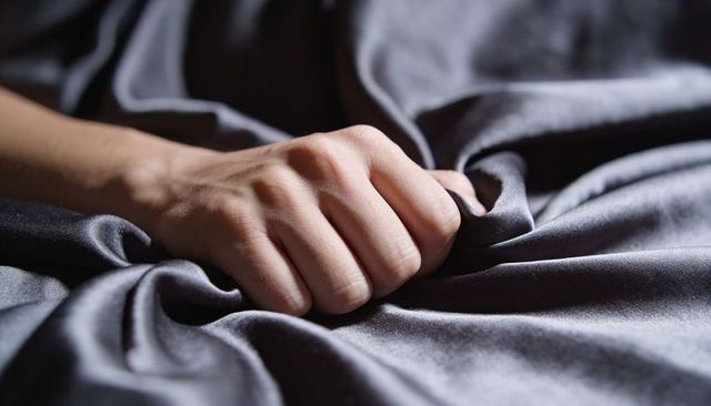 Clutching hand pulling dark gray satin sheet closeup tactile fabric folds and creases