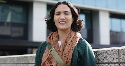Young woman smiling in urban environment wearing cozy knit scarf and crossbody bag