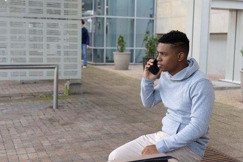 Young african american man talking on phone on urban bench wearing gray hoodie
