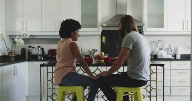 Young couple engaging in a cheerful conversation while seated at a modern kitchen island. Ideal for use in articles or advertisements focused on relationships, domestic lifestyle, modern kitchen design, and everyday life scenes. Can also illustrate concepts of togetherness, well-being, and contemporary home living.
