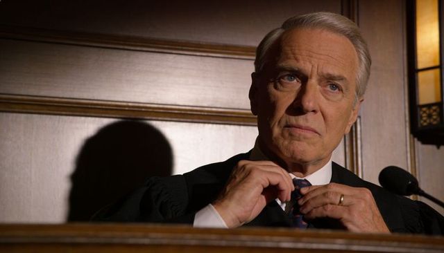 Senior judge adjusting tie at bench under warm courtroom light, thoughtful judicial portrait