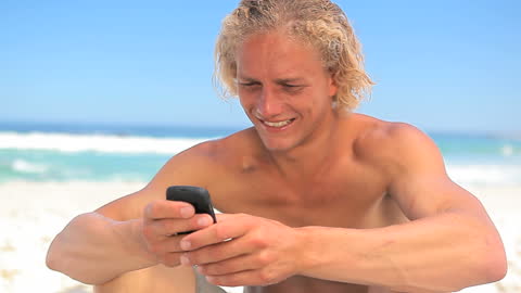 Smiling Blonde Man Texting on Sunny Beach