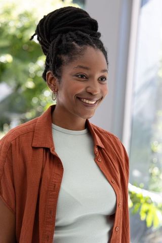 Smiling african woman standing by window wearing rust shirt and mint top, natural light