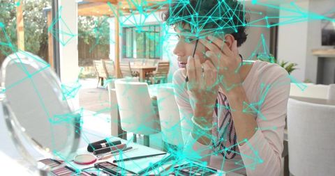Young man applying eye makeup at open-plan table with mirror and turquoise network overlay