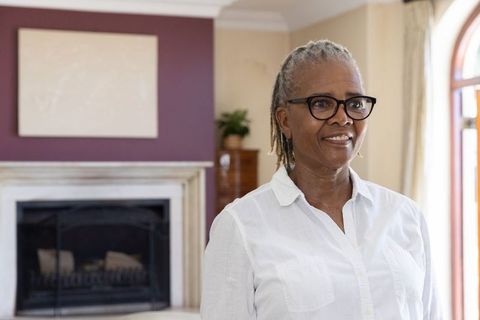 Senior african american woman standing and smiling in elegant living room by fireplace