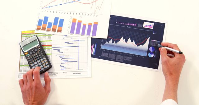 This image shows a person's hands working with financial graphs and using a calculator on a desk. Ideal for articles and presentations on business analysis, finance management, statistical evaluation, financial planning, and data interpretation.