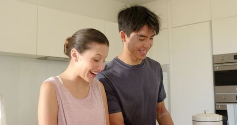 Young couple preparing meal together in modern bright kitchen, smiling and cooking in casual clothes