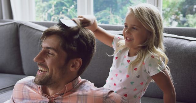 Laughing father and daughter with blonde hair brushing hair on gray sofa - Download Free Stock Images Pikwizard.com