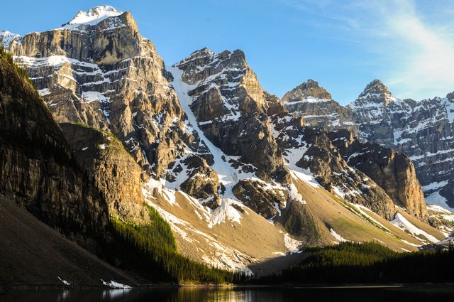 Snow-capped mountain peaks basked in sunlight, reflecting in an undisturbed lake. Suitable for travel brochures, nature blogs, desktop wallpapers, and environmental campaigns.