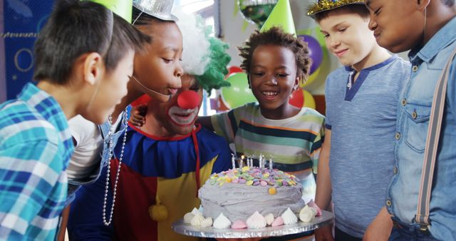 A diverse group of children is gathered around a birthday cake, with a person dressed as a clown entertaining them, with copy space. Capturing the joy and excitement of a child's birthday party, the image reflects a moment of celebration and fun.