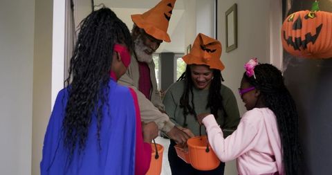 African-american family celebrating halloween at front door handing candy to children