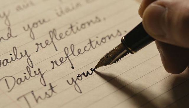 Fountain pen writing daily reflections in cursive on lined notebook page, warm sepia close-up