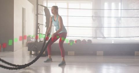 Woman training with battle ropes in minimalist boxing studio with backlit ring silhouette