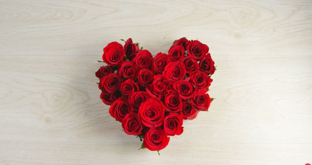 Heart-shaped arrangement of red roses on light wooden surface. Perfect for Valentine's Day promotions, romantic greeting cards, floral advertisements and elegant home decor concepts.