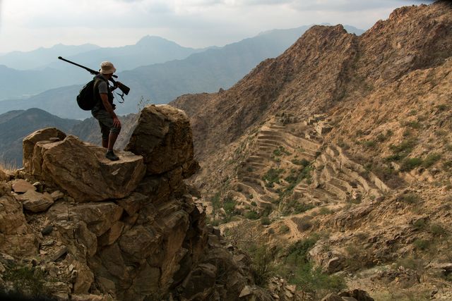Photographer standing on rocky outcrop, capturing breathtaking mountain views. Ideal for use in travel blogs, outdoor adventure promotions, backpacking tips, and nature photography portfolios.