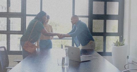 Business colleagues shaking hands over conference table in bright minimalist boardroom
