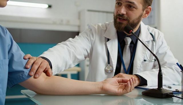 Male doctor comforting patient during consultation with hand on arm stethoscope microphone