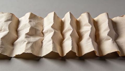 Accordion-pleated beige canvas strip showing woven texture, folds, studio lighting shadows