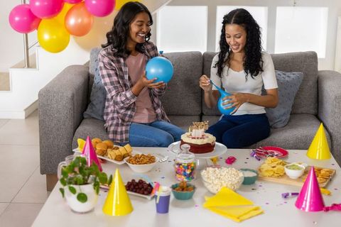Friends inflating balloons and arranging cake for cozy home birthday party