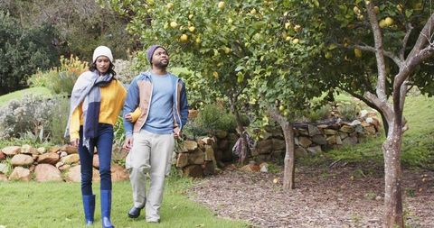 Couple walking arm-in-arm through citrus orchard wearing boots and cozy fall layers