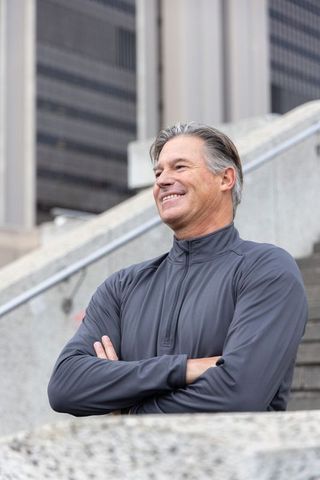 Confident middle-aged man standing on urban steps smiling with arms crossed