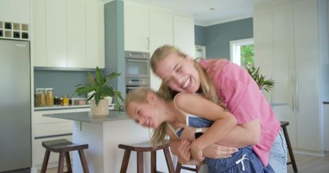 Playful mother hugging daughter in modern kitchen celebrating family bonding and joy