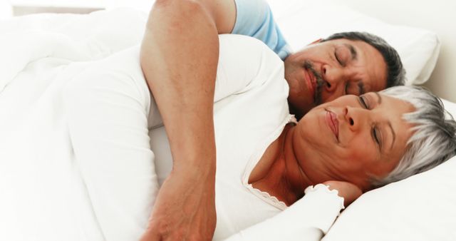 A middle-aged Caucasian couple is peacefully sleeping together, embracing in a comfortable bed, with copy space. Their relaxed expressions and close proximity convey a sense of intimacy and trust in their relationship.
