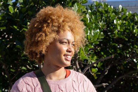 Sunlit african american woman smiling blonde curly hair wearing pink knit sweater