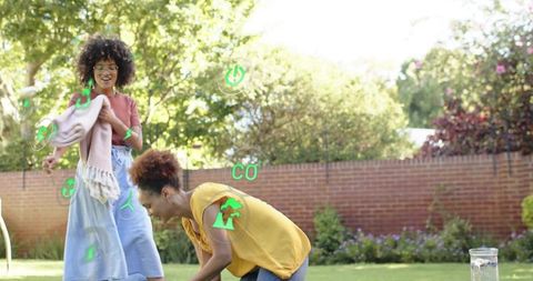 Friends arranging picnic blanket on lawn with augmented reality eco and energy icons