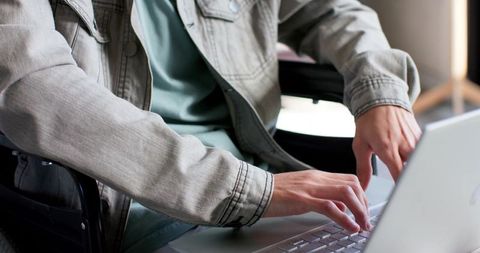 Man typing on silver laptop keyboard and trackpad in casual denim jacket modern workspace close-up