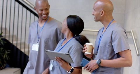Diverse medical team chatting and collaborating in scrubs with tablet and coffee