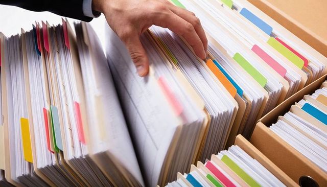 Suit-sleeved hand organizing color-tabbed manila file folders for office records