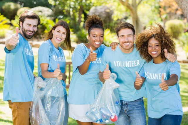 Group of diverse volunteers enjoying time together in a park while participating in a cleanup activity. They are smiling and giving thumbs up, holding bags of collected recyclables. Ideal for use in campaigns promoting community service, environmental awareness, teamwork, and social responsibility.