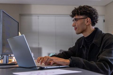 Asian young professional working on laptop with external monitor in minimalist workspace
