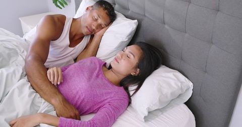Couple sleeping peacefully in modern bed cuddling under white sheets with cozy headboard