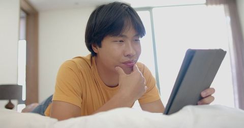 Asian Student Engaged with Tablet on Bed, Casual Home Interior