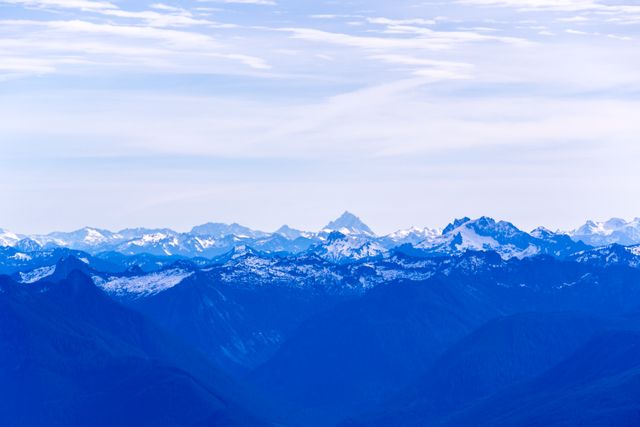 Capturing blue-hued mountain ranges under a partly cloudy sky, this serene landscape photo portrays distant mountains with a peaceful and tranquil setting. Perfect for use in travel brochures, nature calendars, wallpaper backgrounds, environmental conservation materials, or inspirational posters promoting adventure and outdoor activities.
