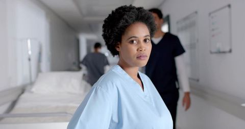 Confident nurse in hospital corridor amidst healthcare professionals