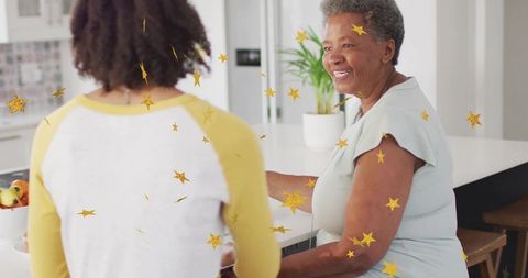 Smiling senior woman chatting at bright kitchen island with adult companion and gold stars