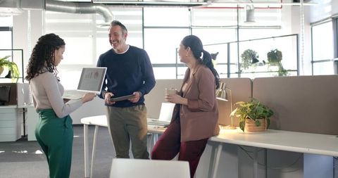 Diverse team presenting laptop chart while collaborating in modern open-plan office