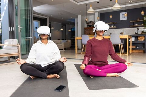 Diverse women practicing virtual reality meditation on yoga mats in modern living room